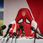 Persruimte in AS Monaco-sfeer met lege trainersstoel en microfoons rond een mogelijke trainersaanstelling