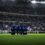 Japanse spelers vormen een kring voor een interland met supporters en stadionlicht op de achtergrond.
