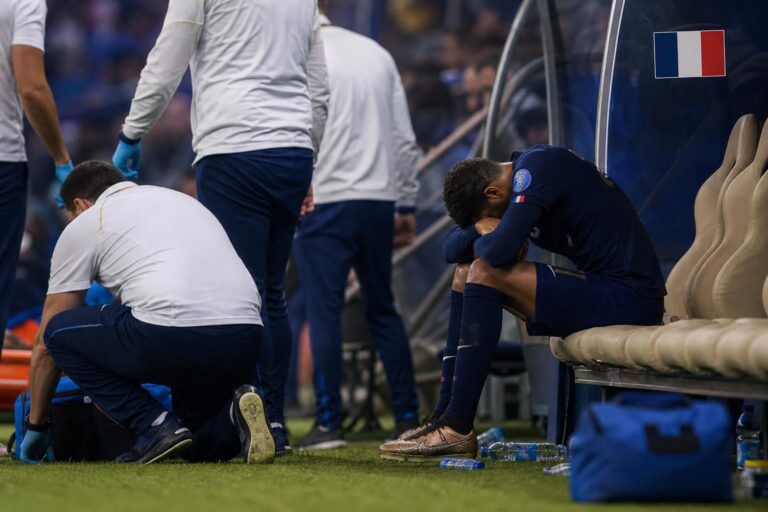 Een aangeslagen speler in Franse wedstrijdcontext zit na een blessuremoment aan de zijlijn, zonder herkenbare gezichten.