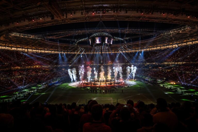 Een fel verlicht stadion tijdens een WK-rustshow met volle tribunes en showlichten