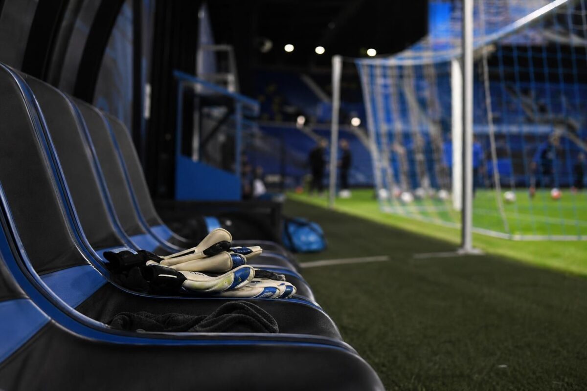 Goalkeepershandschoenen naast een bank in een blauw-zwarte stadionomgeving bij Club Brugge