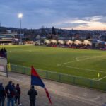 Het veld en de compacte tribunes van Stade de Rocourt, met rood-marineblauwe accenten die verwijzen naar RFC Liège.