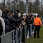 Supporters en spelers rond een Vlaams voetbalveld in een geladen sfeer zonder herkenbare gezichten