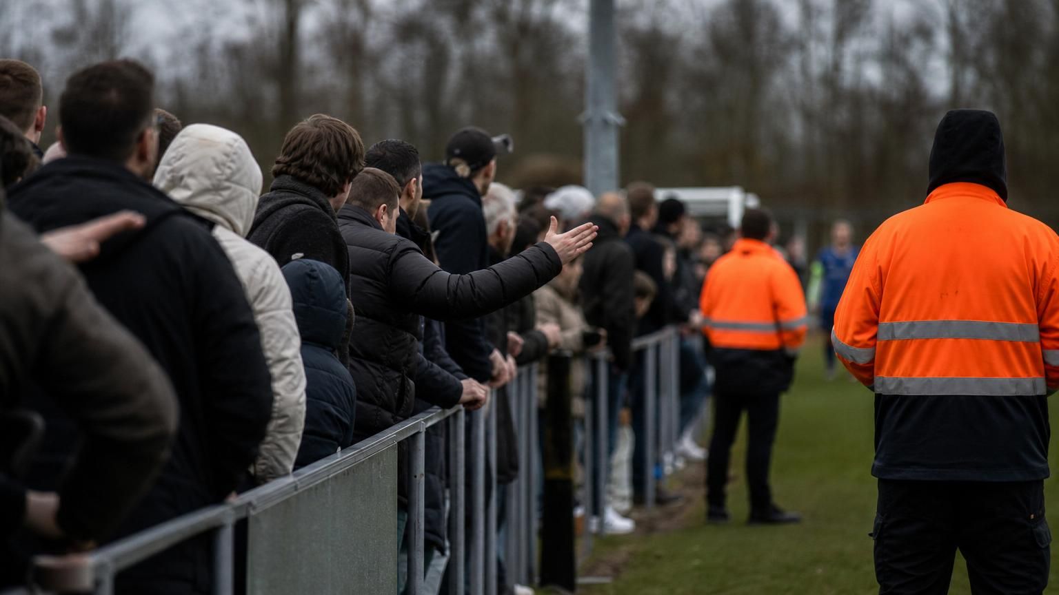 Supporters en spelers rond een Vlaams voetbalveld in een geladen sfeer zonder herkenbare gezichten