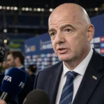 Gianni Infantino staat met ernstige blik in de mediazone van een WK-stadion