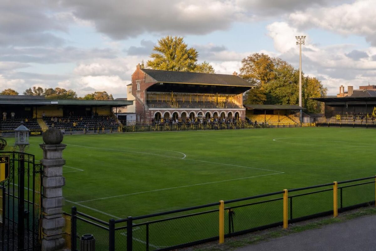 Het Ludo Coeckstadion van Berchem Sport met het veld, bescheiden tribunes, historische poort en geel-zwarte accenten.