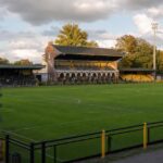 Het Ludo Coeckstadion van Berchem Sport met het veld, bescheiden tribunes, historische poort en geel-zwarte accenten.
