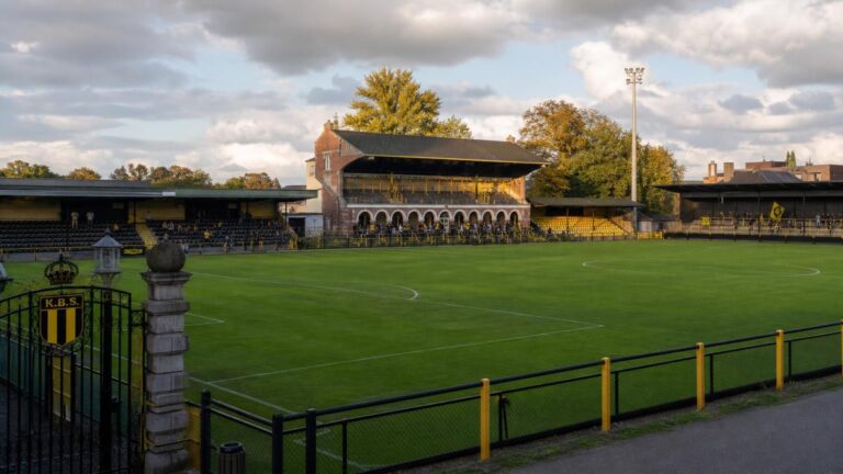 Het Ludo Coeckstadion van Berchem Sport met het veld, bescheiden tribunes, historische poort en geel-zwarte accenten.