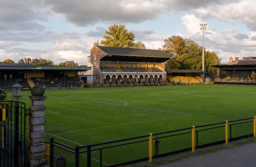 Het Ludo Coeckstadion van Berchem Sport met het veld, bescheiden tribunes, historische poort en geel-zwarte accenten.