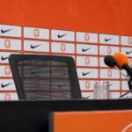 Een lege persstoel met microfoons in een Oranje-context tijdens discussie over de bondscoachpositie