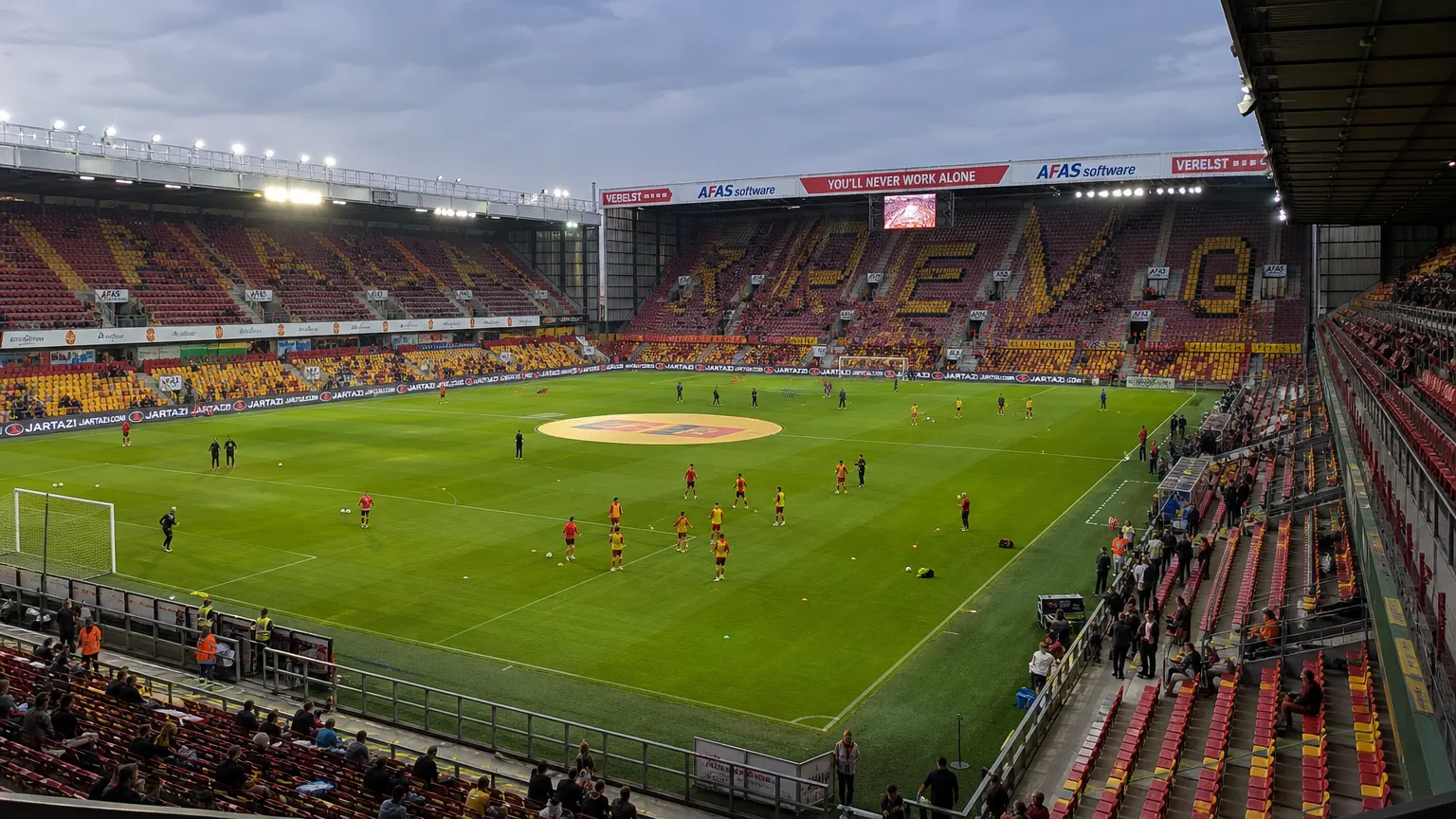 Spelers van KV Mechelen warmen in groep op in een gevuld stadion