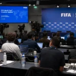 Journalisten in een internationale voetbalpersruimte met FIFA-branding op de achtergrond