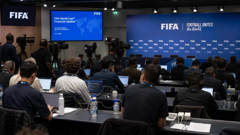Journalisten in een internationale voetbalpersruimte met FIFA-branding op de achtergrond