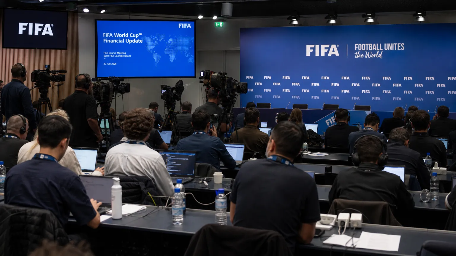 Journalisten in een internationale voetbalpersruimte met FIFA-branding op de achtergrond