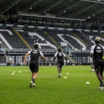 Breed wedstrijddagbeeld van het stadion van Sporting Charleroi met een opwarmende spelersgroep.