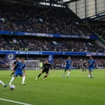 Niet-identificeerbare Chelsea-spelers in blauw tenue tijdens een wedstrijd in een gevuld stadion.