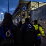 Transfercontext rond Club Brugge met stadionlichten en blauw-zwarte sjaals zonder herkenbare gezichten.