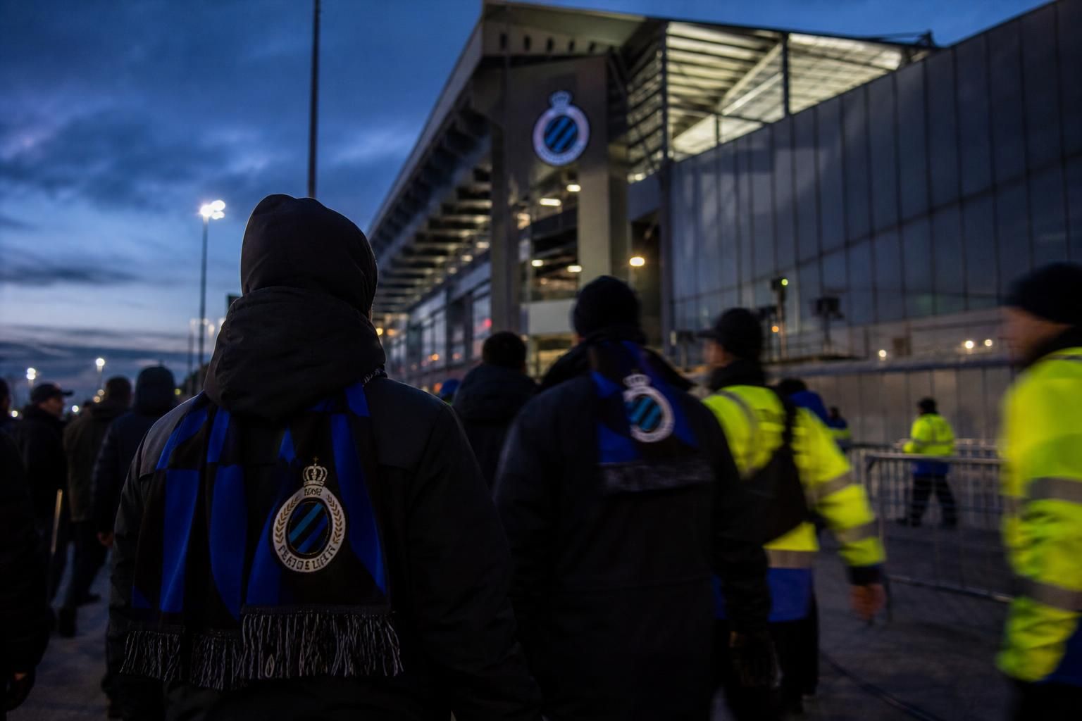 Transfercontext rond Club Brugge met stadionlichten en blauw-zwarte sjaals zonder herkenbare gezichten.
