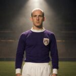 Georges Heylens in het paarse Anderlecht-tenue van de late jaren zestig onder een stadionspot.