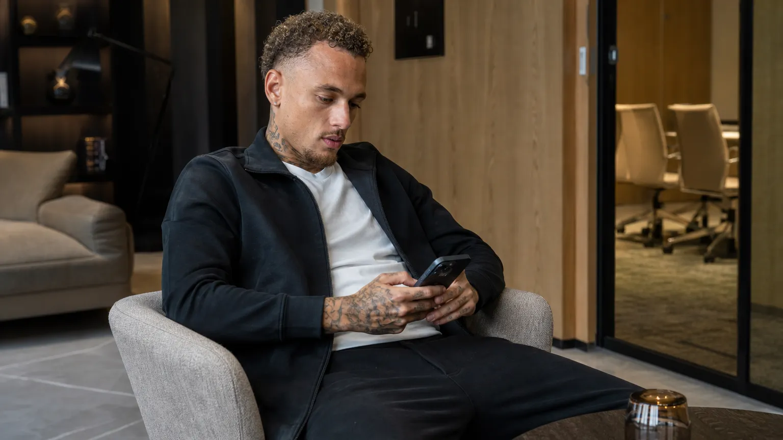 Noa Lang in neutrale sportkleding in een rustige hotellounge.