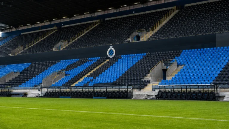 Een lege blauw-zwarte tribune met een Club Brugge-embleem aan de rand van het veld.