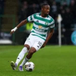 Michel-Ange Balikwisha in een groen-wit gestreept tenue op een nat voetbalveld.