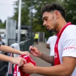 Tristan Gooijer signeert een shirt voor supporters aan een afsluiting.