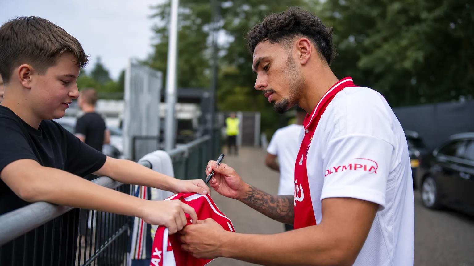 Tristan Gooijer signeert een shirt voor supporters aan een afsluiting.