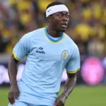 Mohammed Fuseini kijkt geconcentreerd naar het spel op een voetbalveld in een lichtblauw tenue.
