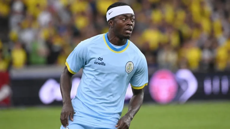 Mohammed Fuseini kijkt geconcentreerd naar het spel op een voetbalveld in een lichtblauw tenue.