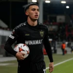 Bilal El Khannouss in een donker voetbaltenue langs de zijlijn van een stadion.