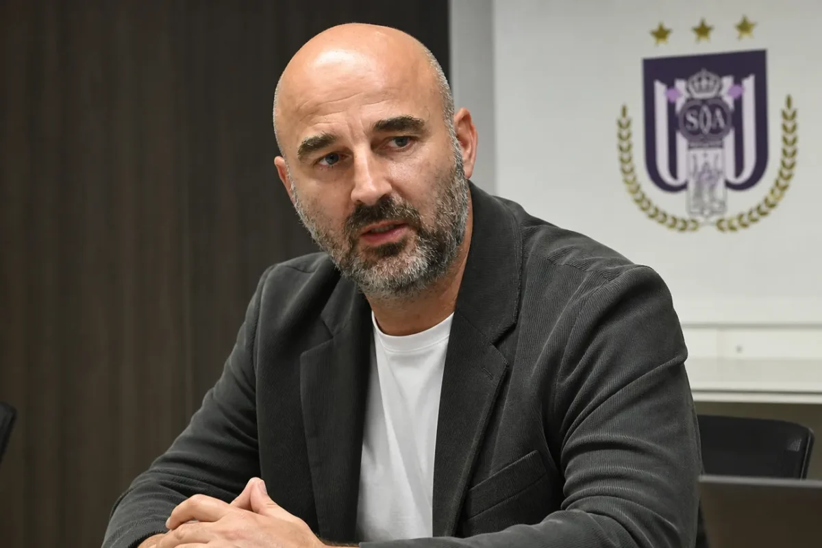 Antoine Sibierski zit aan een mediatable in een ruimte met een discreet RSC Anderlecht-wanddetail.