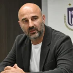 Antoine Sibierski zit aan een mediatable in een ruimte met een discreet RSC Anderlecht-wanddetail.