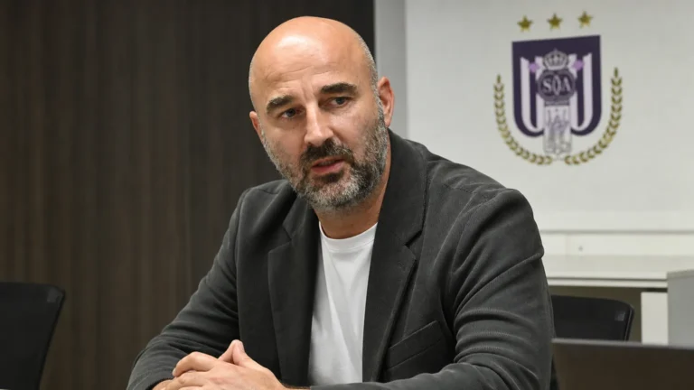 Antoine Sibierski zit aan een mediatable in een ruimte met een discreet RSC Anderlecht-wanddetail.