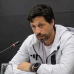 Vitor Bruno spreekt tijdens een voetbalmedia briefing aan een tafel met microfoon.