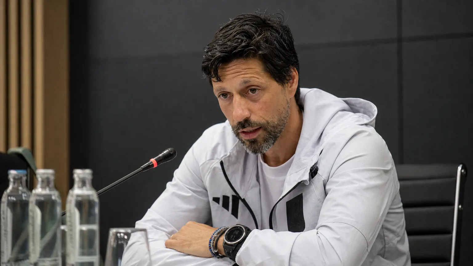 Vitor Bruno spreekt tijdens een voetbalmedia briefing aan een tafel met microfoon.