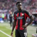 Ernest Poku tijdens een rustig moment langs de zijlijn in zijn zwart-rode tenue.