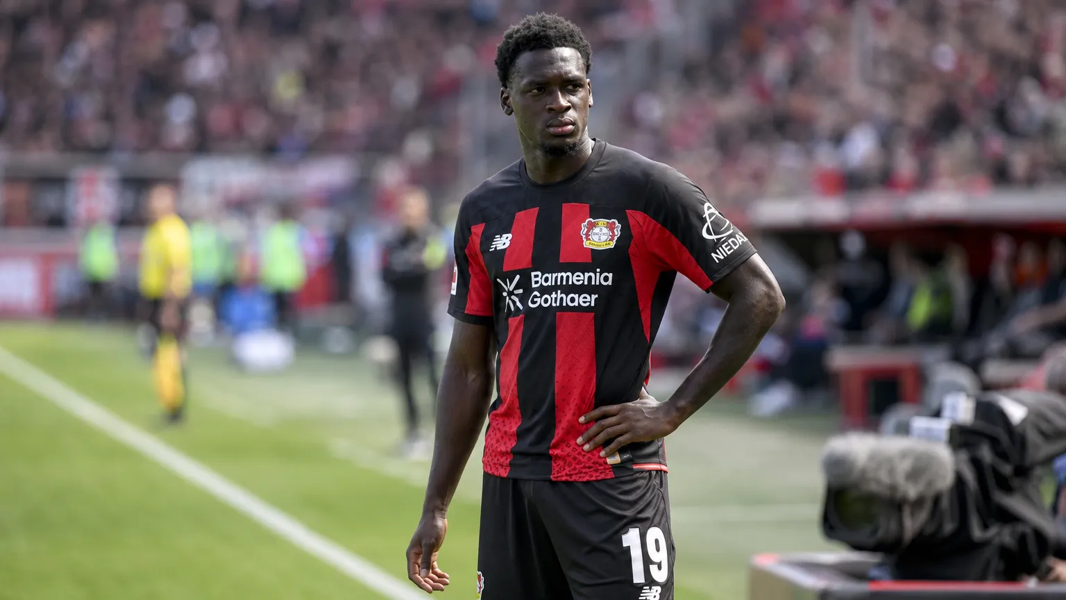 Ernest Poku tijdens een rustig moment langs de zijlijn in zijn zwart-rode tenue.