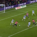 Spelers in rood-wit gestreepte en lichtblauwe tenues strijden om de bal nabij het strafschopgebied.