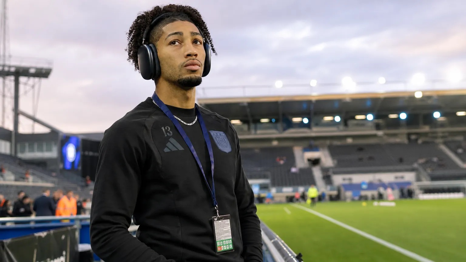Nathan-Dylan Saliba in zwarte sportkleding aan de zijlijn van een voetbalstadion.