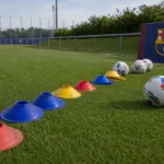 Trainingsmateriaal op een oefenveld met een discreet FC Barcelona-bord langs de zijlijn.