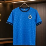 Het blauwe derde shirt van Club Brugge hangt aan een metalen hanger in een verlichte clubruimte.
