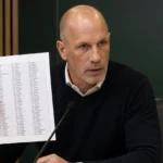 Philippe Clement houdt tijdens een persconferentie een blad met een landenlijst vast voor een Norwich City-achtergrond.