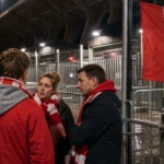 Standard-supporters verzamelen zich rustig aan een stadioningang na een avondwedstrijd.