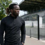 Parfait Guiagon in neutrale sportkleding bij een voetbalstadion.