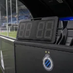 Verlichte technische zone van Club Brugge naast het veld tijdens een avondwedstrijd.
