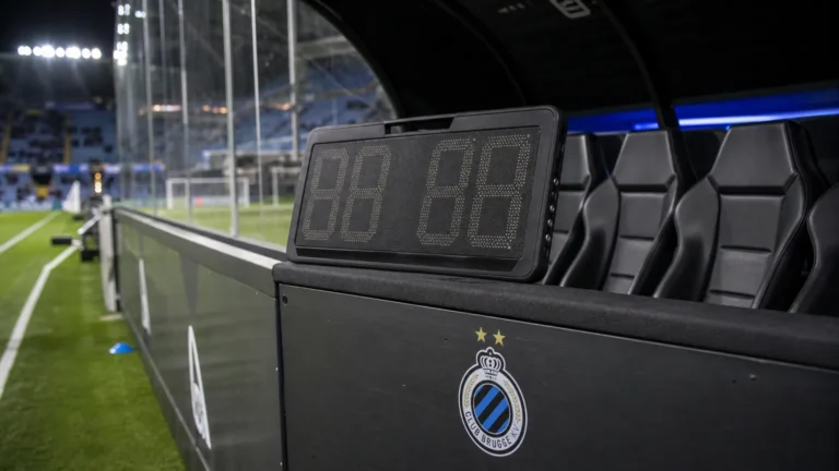 Verlichte technische zone van Club Brugge naast het veld tijdens een avondwedstrijd.