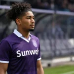 Nathan-Dylan Saliba in een paars voetbalshirt langs de zijlijn van een stadion.