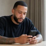 Memphis Depay kijkt op zijn smartphone terwijl hij een verklaring voorbereidt.