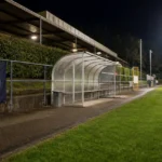 Een verlicht voetbalveld in een klein stadion na het laatste fluitsignaal, met een Sporting Hasselt-vlag langs de zijlijn.